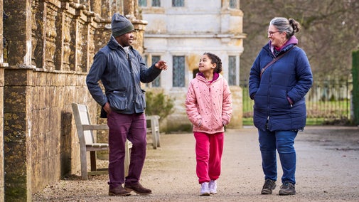 A family of three talking and walking past a balustraded wall at Montacute House
